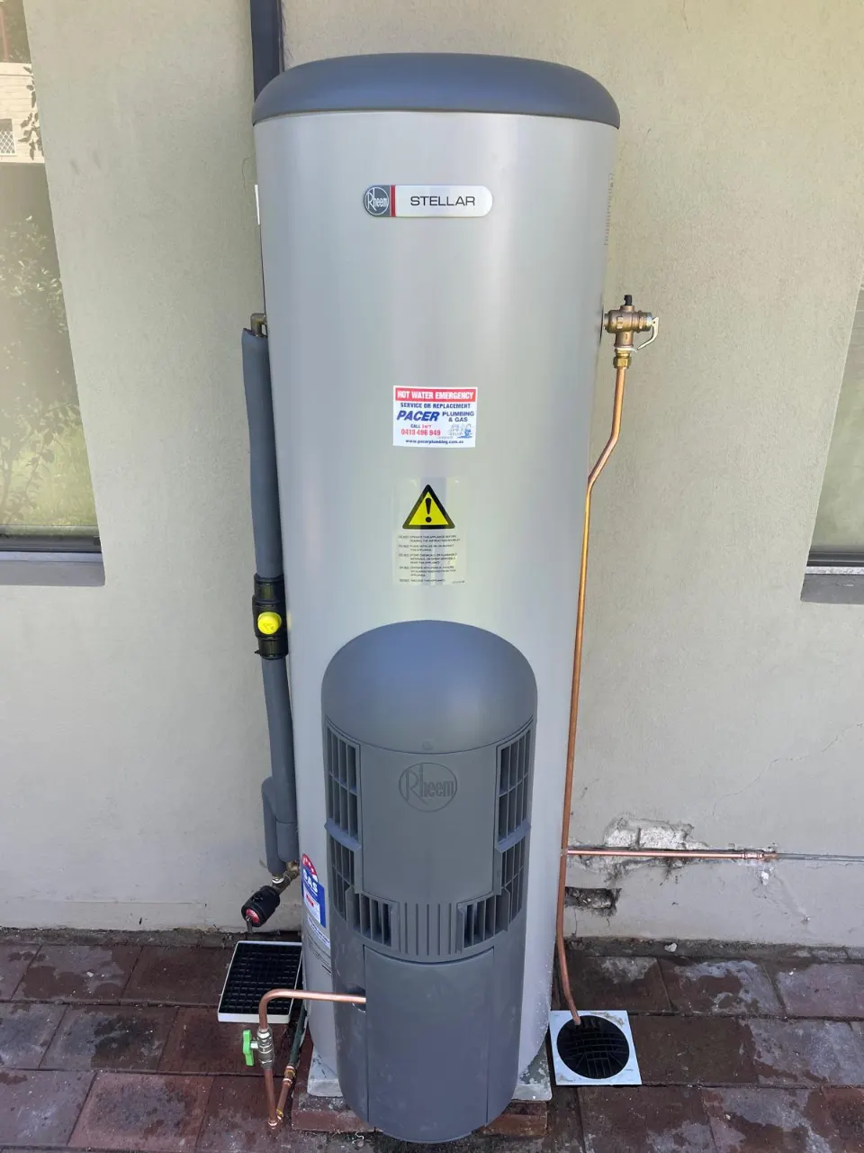 Front view of the installed Rheem Stellar gas storage hot water system with a copper pressure-relief line running to a drain