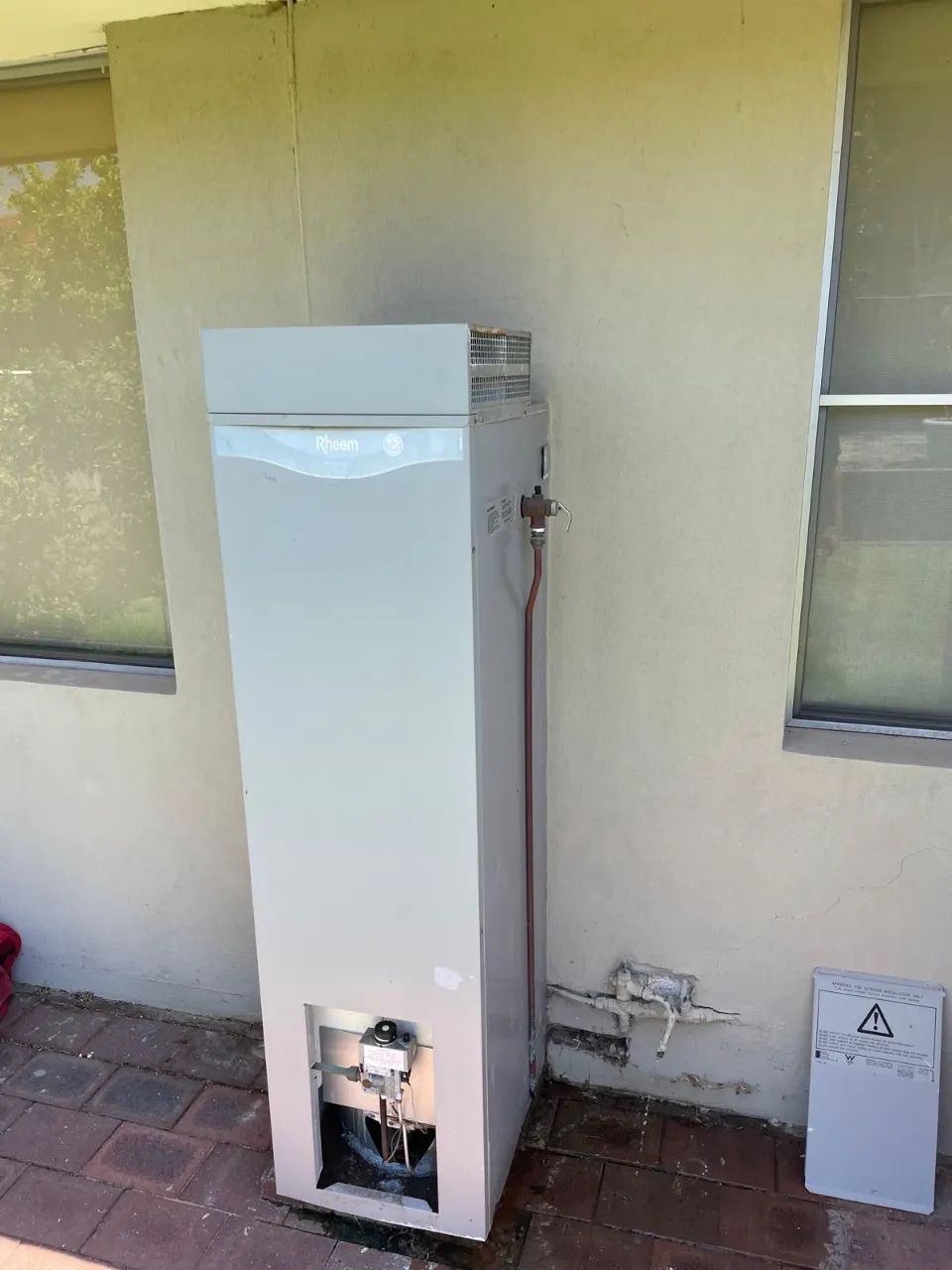 Old hot water heater against an outside wall, before replacement