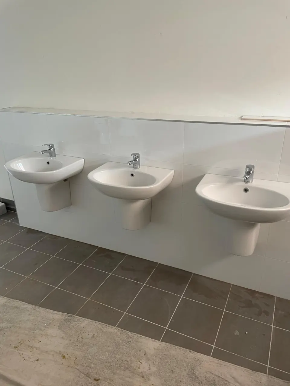 Three wall-hung hand basins with taps on a white tiled wall