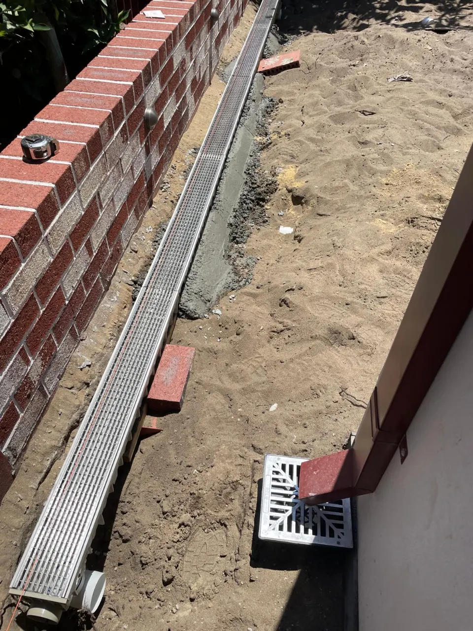 Grated channel drain laid beside a brick wall with a floor waste at the end