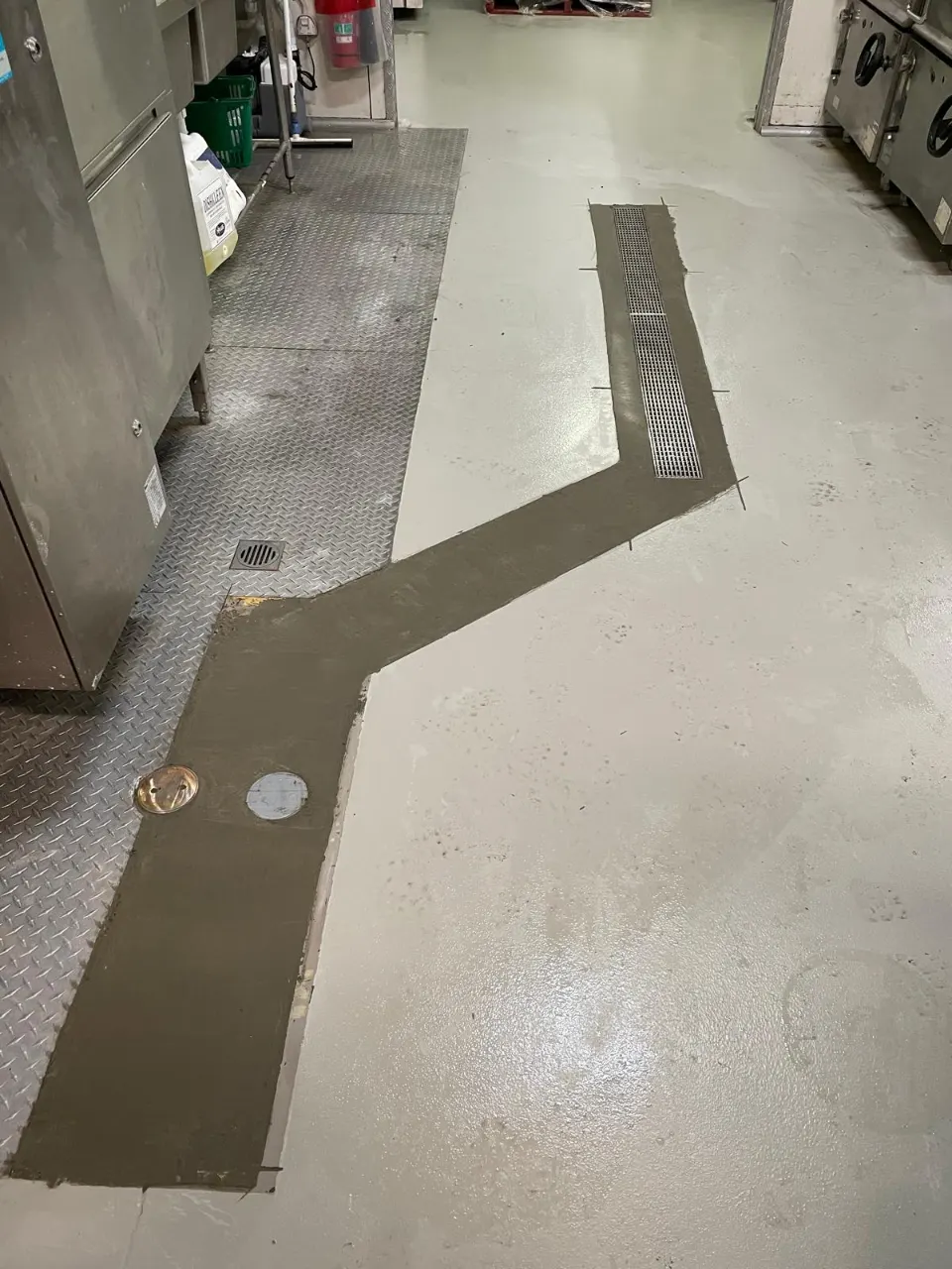 Finished grated channel drain in a commercial kitchen floor with fresh concrete patching