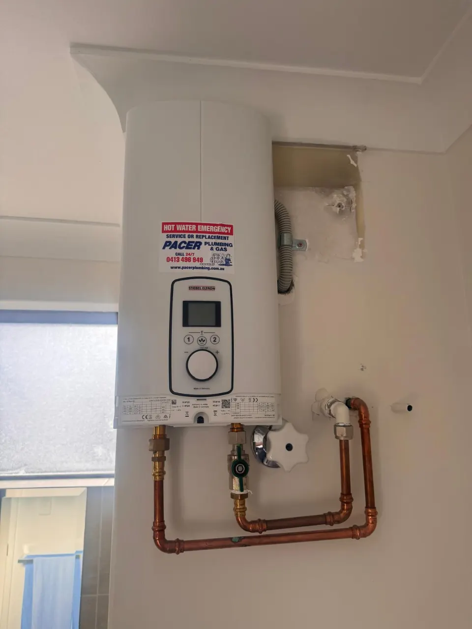 Wall-mounted instant electric hot water unit with a digital display and copper pipework