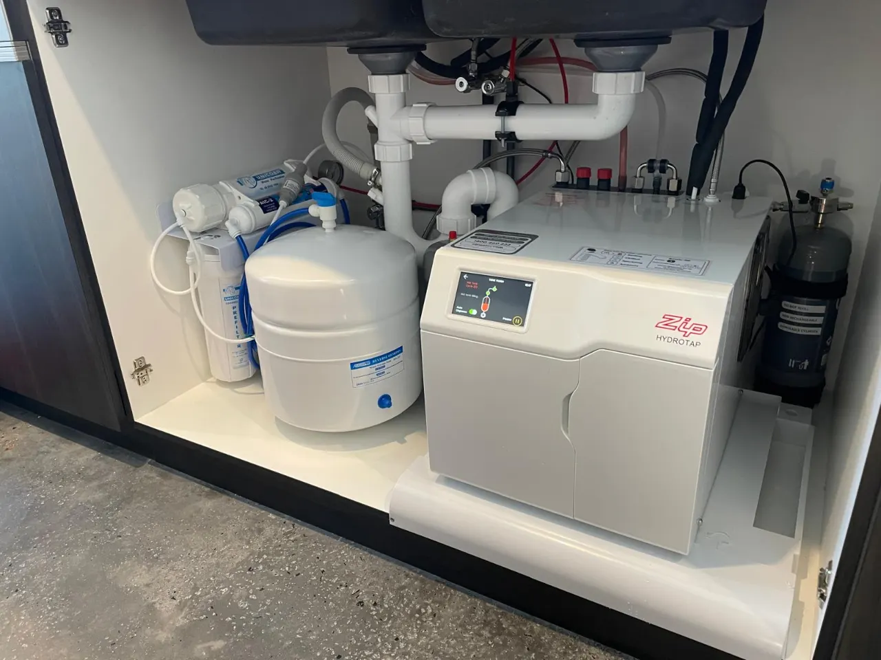 Under-sink water filtration system with a storage tank and a Zip hot water unit inside a cabinet