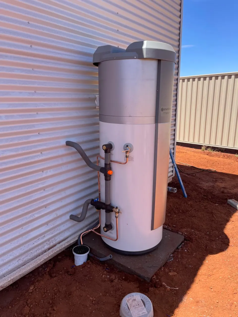 Heat pump hot water system on a concrete pad beside a corrugated metal wall