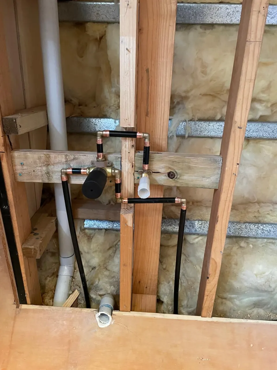 Plumbing rough-in in an insulated wall frame, with copper fittings, a valve and a PVC waste pipe