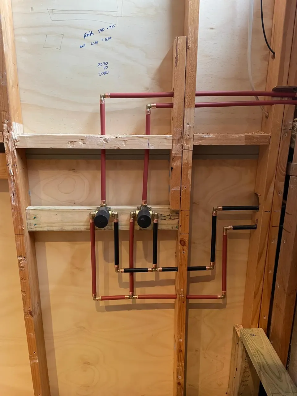 Hot and cold water rough-in pipework in a timber wall frame, red and black pipes with copper fittings and valves