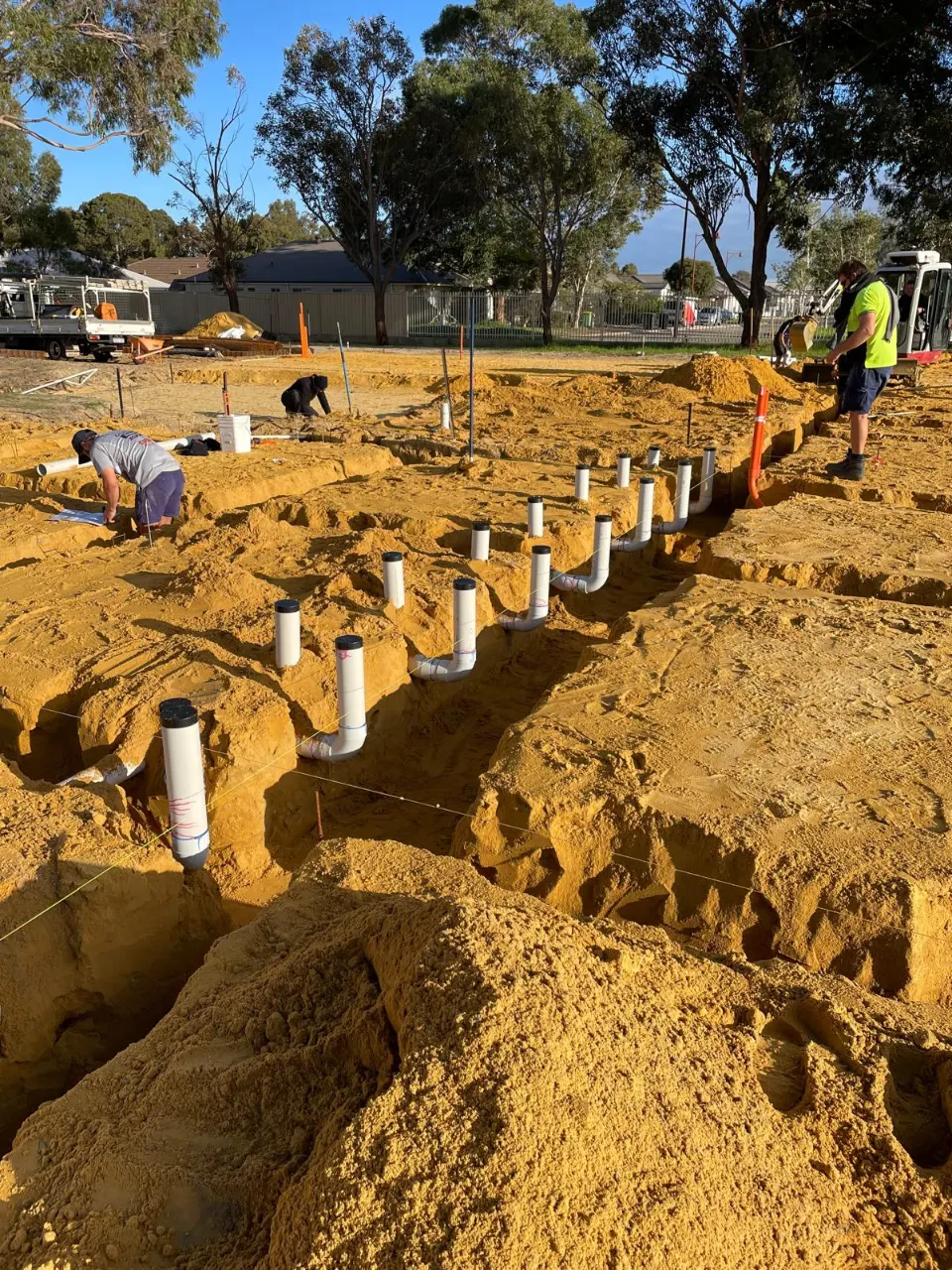Rows of white PVC drainage risers and bends in an excavated trench on a building site