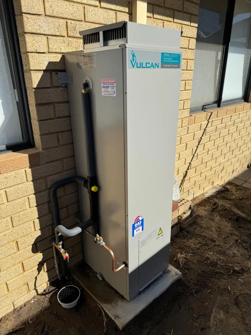 Vulcan gas storage hot water system installed on a brown brick wall, with insulated hot water pipework and copper fittings